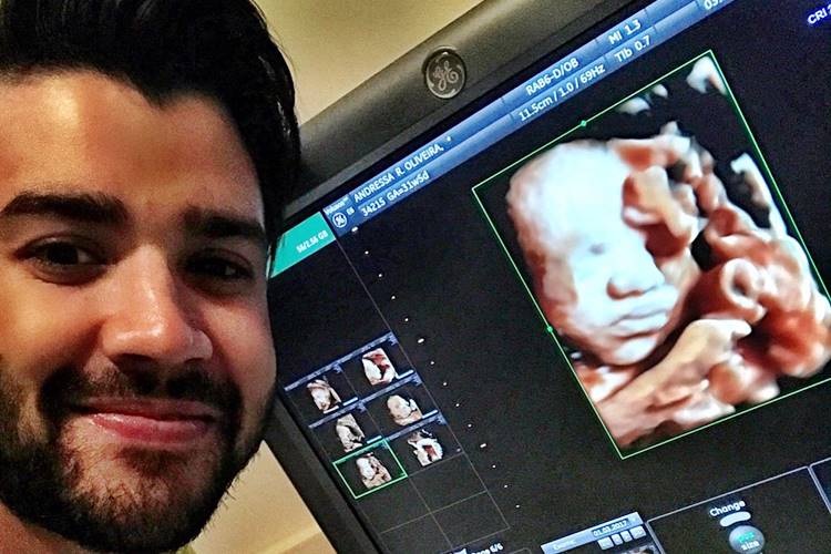 Gusttavo Lima posa sorridente e mostra ultrassom do filho